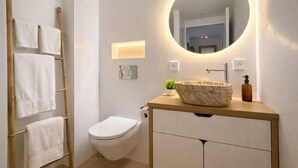 Ein modernes Badezimmer mit einem hölzernen Waschtisch, einem runden Spiegel, einer Toilette und einem Handtuchhalter mit mehreren Handtüchern.