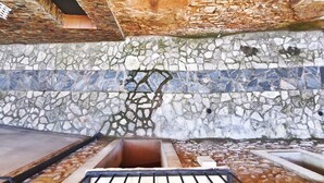 Uma parede de pedra com mosaicos, um banco de madeira e um pequeno espelho d'água.