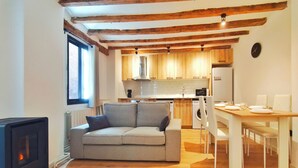 Um espaço compacto com sofá, mesa de jantar e cozinha, com vigas de madeira aparentes e uma janela.