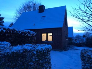 A snow-covered house with a visible window and a chimney.