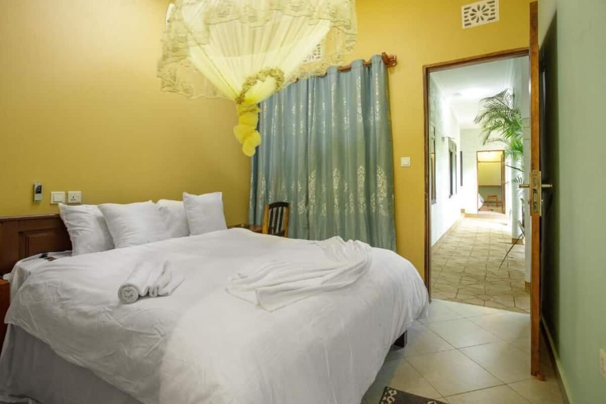 A neatly made bed with white linens, a wooden headboard, and a decorative fan above it.
