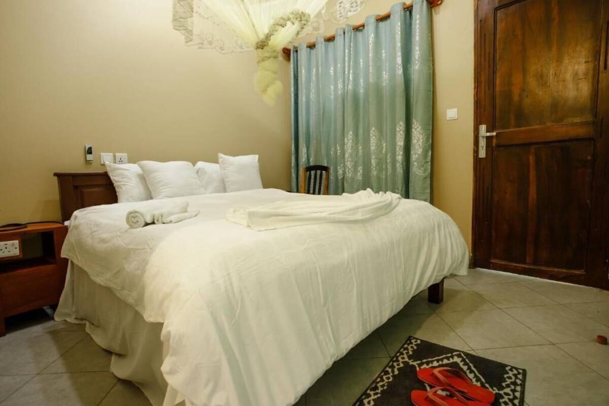 A neatly made bed with white linens, a wooden nightstand with a lamp, a chair, and a door.