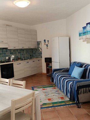 Un espacio habitable compacto con kitchenette, un sofá, una mesa de comedor con sillas y una alfombra colorida.