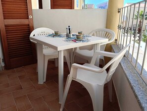 Un balcón con una mesa y sillas blancas, una cafetera y una taza.