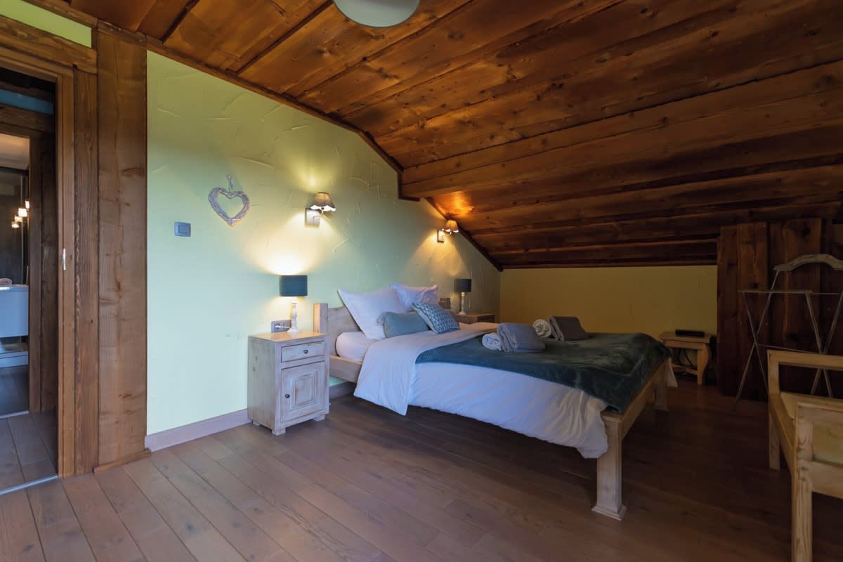 Ein Schlafzimmer mit Holzbalkendecke, einem Bett mit Kissen und Decke, einem Nachttisch mit Lampe und einer herzförmigen Dekoration an der Wand.