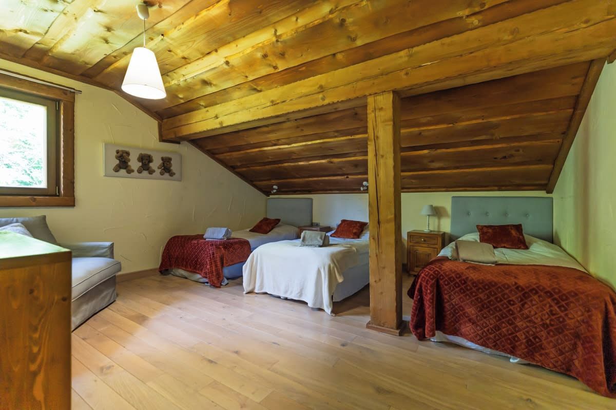 Une pièce avec un plafond en pente, des poutres en bois, deux lits avec une literie rouge, un canapé, un bureau et une fenêtre.