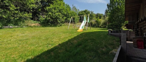 A grassy outdoor area with a swing set and a wooden cabin.