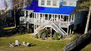 Een woonhuis met twee verdiepingen, een blauw dak, een overdekte veranda en een trap naar de bovenverdieping.