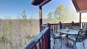 A wooden deck with a table and chairs, overlooking a forested landscape. - Smoky Mountain View (Sevierville)