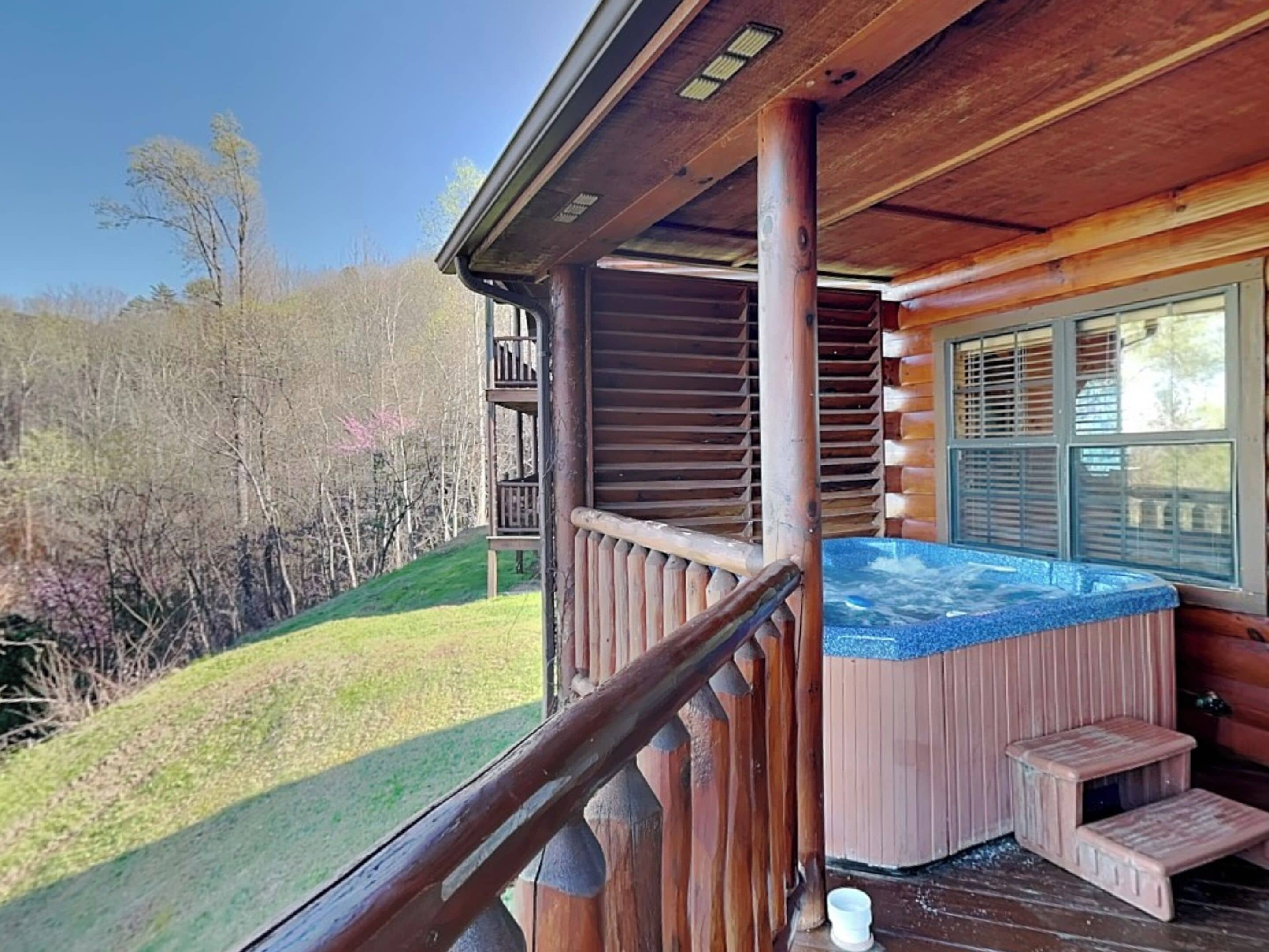 Une cabane en bois dotée d’un bain à remous, d’un balcon et offrant une vue sur la forêt environnante.