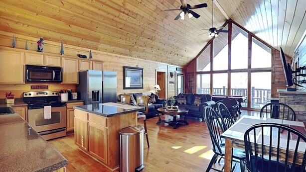 A spacious kitchen with wooden cabinets, a central island, and a dining area with a view. - Smoky Mountain View (Sevierville)