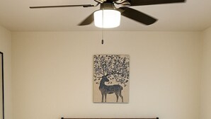 A bedroom with a bed, a ceiling fan, a wall-mounted artwork of a deer, and a dark-colored rug. - Cabana (Miami)