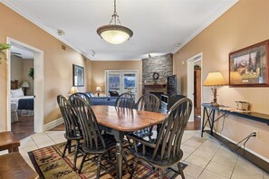 A dining area with a wooden table and chairs, a chandelier, and a stone fireplace. - 🌄Baskins Creek 209 | Foothill Views | Walk to Downtown Gatlinburg🌄 (Gatlinburg)