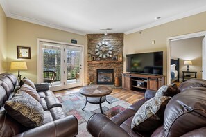A living room with a stone fireplace, leather sofa, and a television. - Baskins Creek 214 🌄 Welcoming Retreat | Pool, Hot Tub & Balcony 🏡 (Gatlinburg)