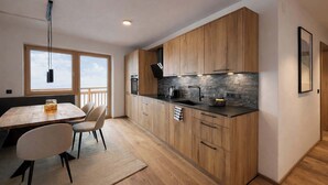 A modern kitchen with wooden cabinets, a stone backsplash, and a dining area with a table and chairs.