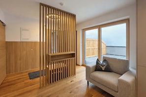 Ein modernes Interieur mit einer Holzwand, einer Couch mit einem Zierkissen und Blick auf eine Holzterrasse durch große Fenster.