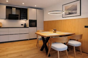 Una cocina moderna con armarios de madera, horno empotrado y comedor con mesa y sillas de madera.