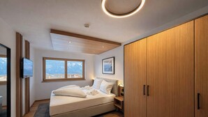 Ein Schlafzimmer mit Bett, Nachttisch, Kleiderschrank und einem großen Fenster mit Blick.