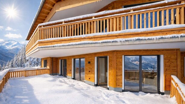 A wooden chalet with a balcony, large sliding glass doors, and a snowy landscape.