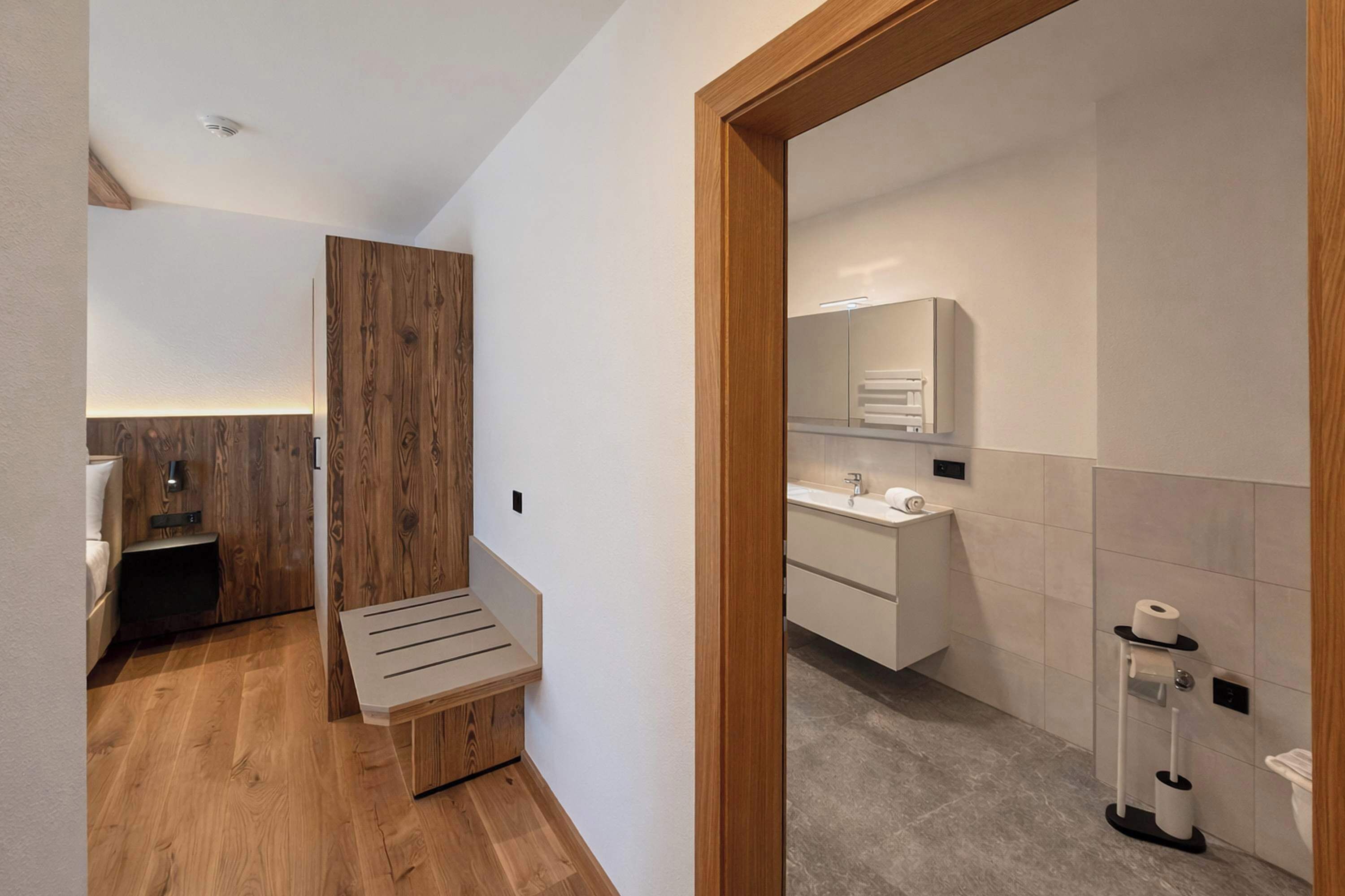 Een moderne badkamer met een houten bankje, een wastafel en een toilet.