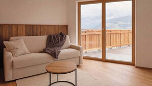 A living room with a sofa, a small round table, and a large sliding glass door leading to a balcony.