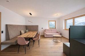 A modern living space with a wooden dining table, pink chairs, a sofa, and a TV.