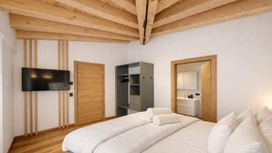 A modern bedroom with a wooden ceiling, a flat-screen TV, a wardrobe, a built-in wardrobe, a mirror, and a bed with white bedding.
