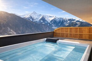 Ein Whirlpool mit Blick auf die Berge, eine Holzdar Terrasse und ein klarer Himmel.