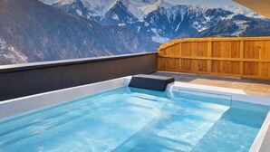 A hot tub with a mountain view, wooden deck, and a dark wall.