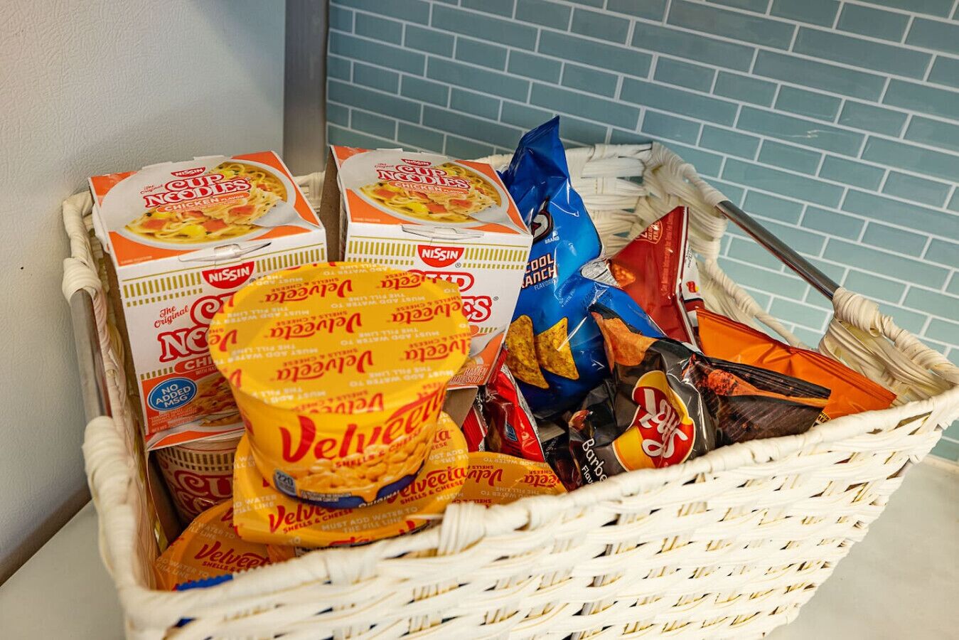 A basket containing food items including Velveeta cheese, Nissin Cup Noodles, and other snacks.