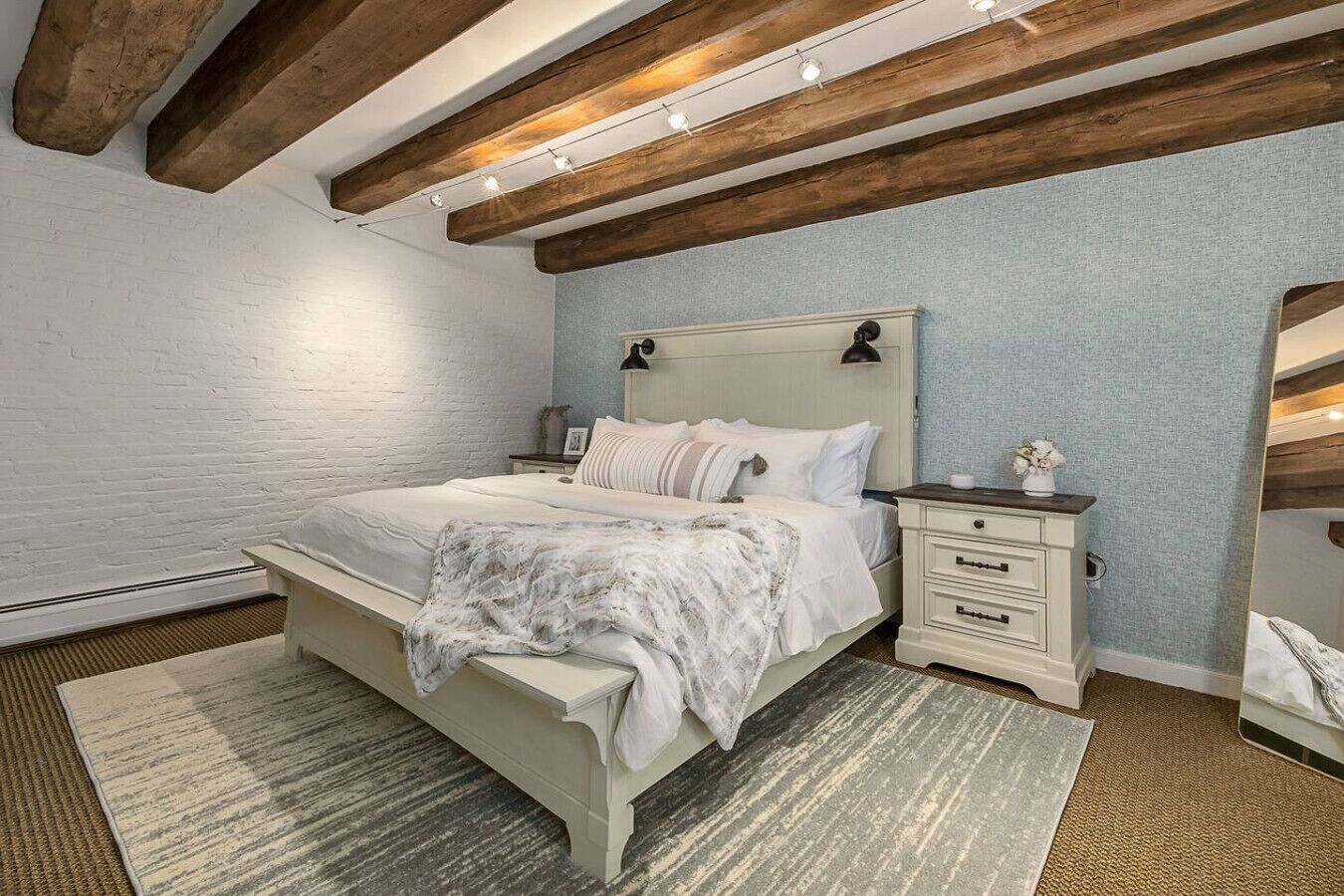 Une chambre à coucher avec un lit, des tables de chevet, une commode, un miroir et un plafond en bois.