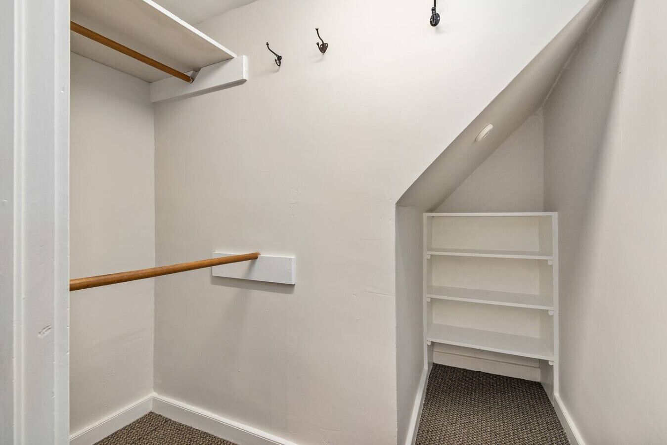 Un pasillo estrecho con barandilla de madera, paredes blancas y un armario blanco con estantes.