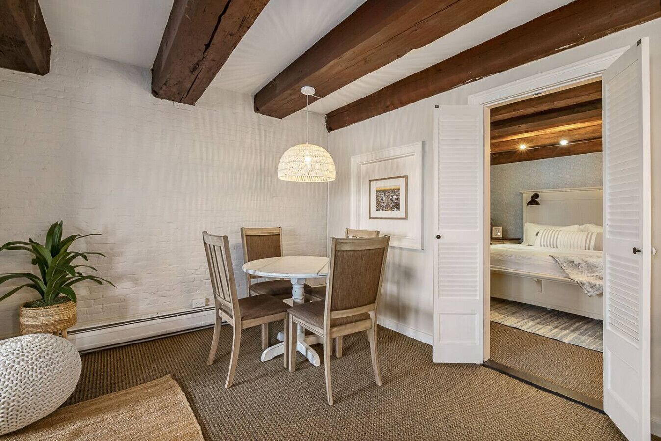 Une pièce comprenant une table à manger, des chaises, un luminaire suspendu, un lit et une porte donnant sur une autre pièce.