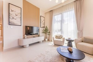Ein modernes Wohnzimmer mit Flachbildfernseher, einer Couch, einem Couchtisch und einer Topfpflanze.
