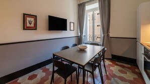 A dining area with a table, chairs, a flat-screen TV, and a window with curtains. - Toscana 4 - FromHometoRome (Roma)