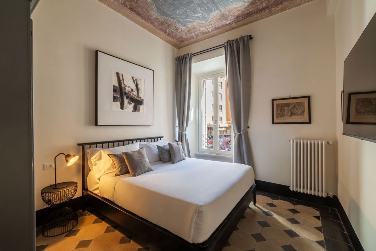 A bedroom with a bed, a nightstand, a radiator, and a window with curtains.