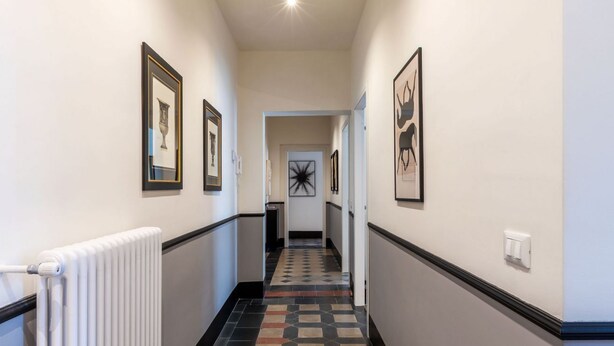 A hallway with framed artwork on the walls, a radiator, and a patterned floor. - Toscana 4 - FromHometoRome (Roma)