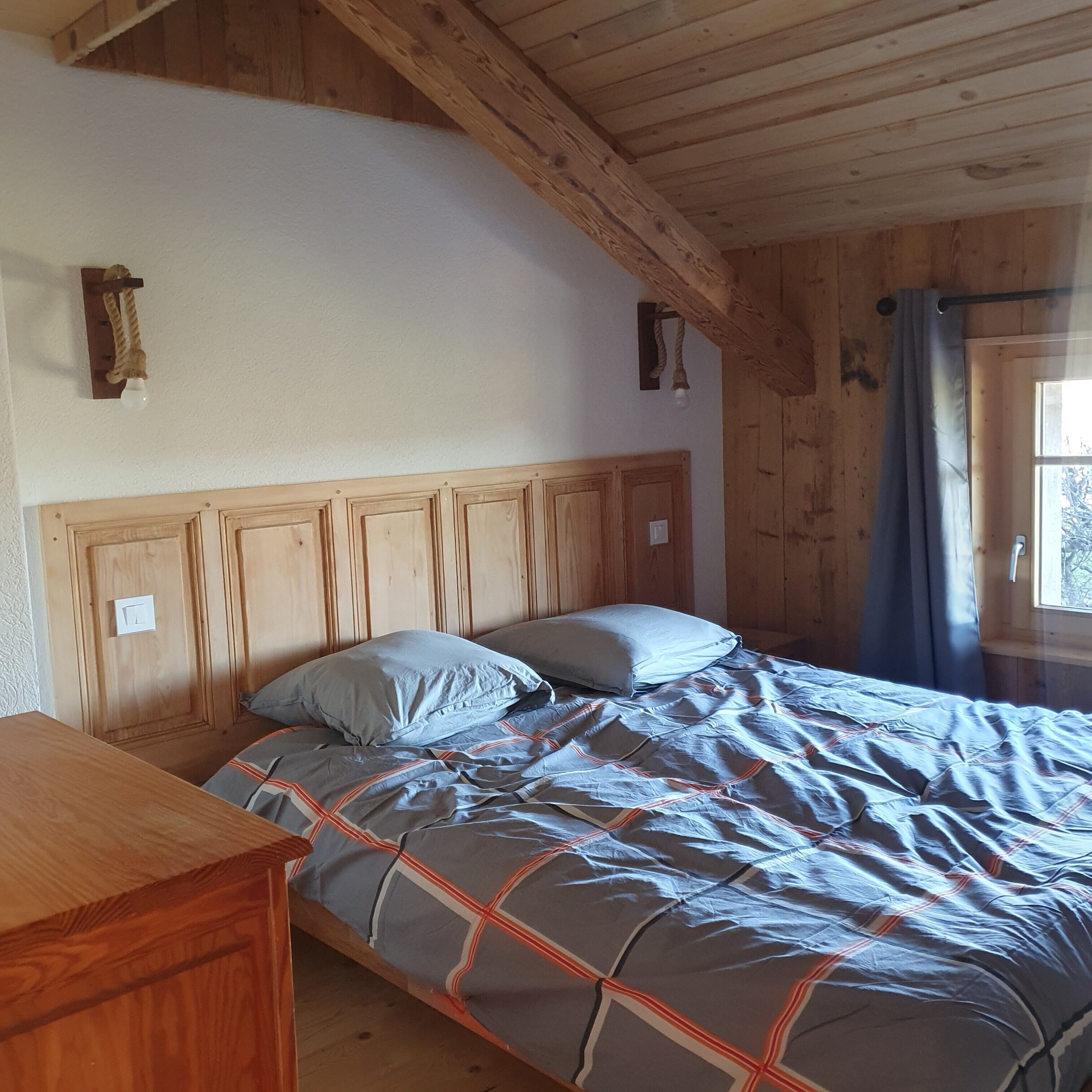 A wooden-paneled bedroom with a bed, pillows, a nightstand, and a window with curtains.
