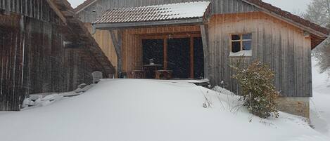 A rustic barn with a snow-covered roof and a wooden door.
