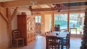 Un intérieur en bois comprenant une table à manger, des chaises, un buffet et une vue sur l’extérieur grâce à une grande fenêtre.