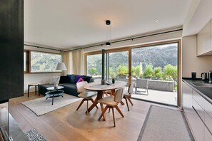 Ein modernes Wohnzimmer mit einem runden Esstisch, einer Couch und Blick auf Berge durch große Fenster.