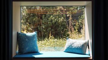 A window seat with two pillows, a view of greenery and a wooden structure outside.