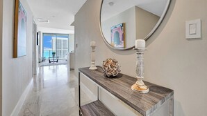 A hallway with a marble floor, a round mirror, a wooden console table, and a view of a balcony with a cityscape. - Spacious 3-bedroom apartment Ocean View in lovely Hallandale Beach (Hallandale Beach)