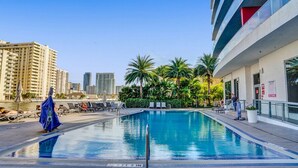 A swimming pool with lounge chairs, palm trees, and a cityscape in the background. - Spacious 3-bedroom apartment Ocean View in lovely Hallandale Beach (Hallandale Beach)