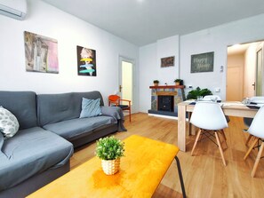 A living room with a sofa, a coffee table with a plant, a dining area with a table and chairs, a fireplace, and artwork on the walls. - Apartment in Vilassar de Mar, Barcelona Coast (Vilassar de Mar)