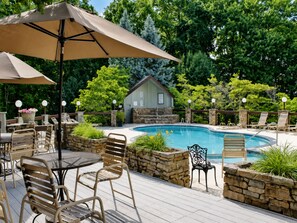 A poolside area with a stone wall, lounge chairs, and a table with chairs. - Gatlinburg Condo*Mtn. Views*Seasonal Resort Amenities (GATLINBURG)