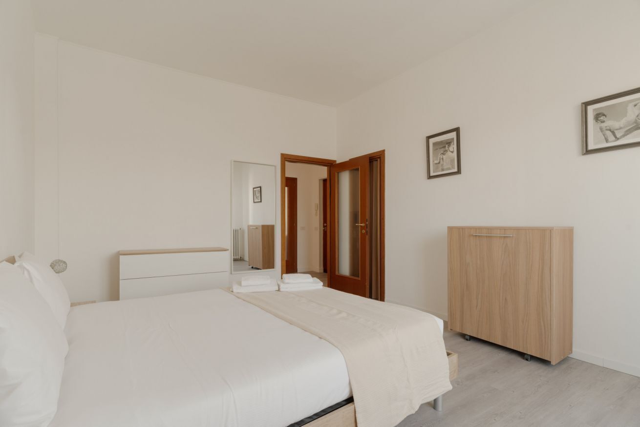 A bedroom with a bed, a wardrobe, a mirror, and a door leading to another room.