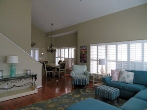 A spacious living room with a staircase, a dining area, and a large window with blinds. - Amazing Sunsets, Sound Front View, Private Dock (Ocean Isle Beach)