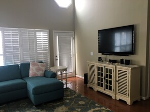 A living room with a sectional sofa, a television on a cabinet, and a door with a window. - Amazing Sunsets, Sound Front View, Private Dock (Ocean Isle Beach)