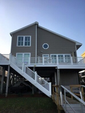 A two-story house with a covered garage, a staircase leading to a deck, and a small octagonal window. - Amazing Sunsets, Sound Front View, Private Dock (Ocean Isle Beach)